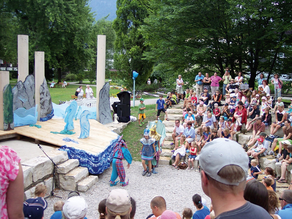 Im Amphitheater im Garmischer Kurpark sitzen zahlreiche Zuschauer und verfolgen das Geschehen vor und auf der Bühne.