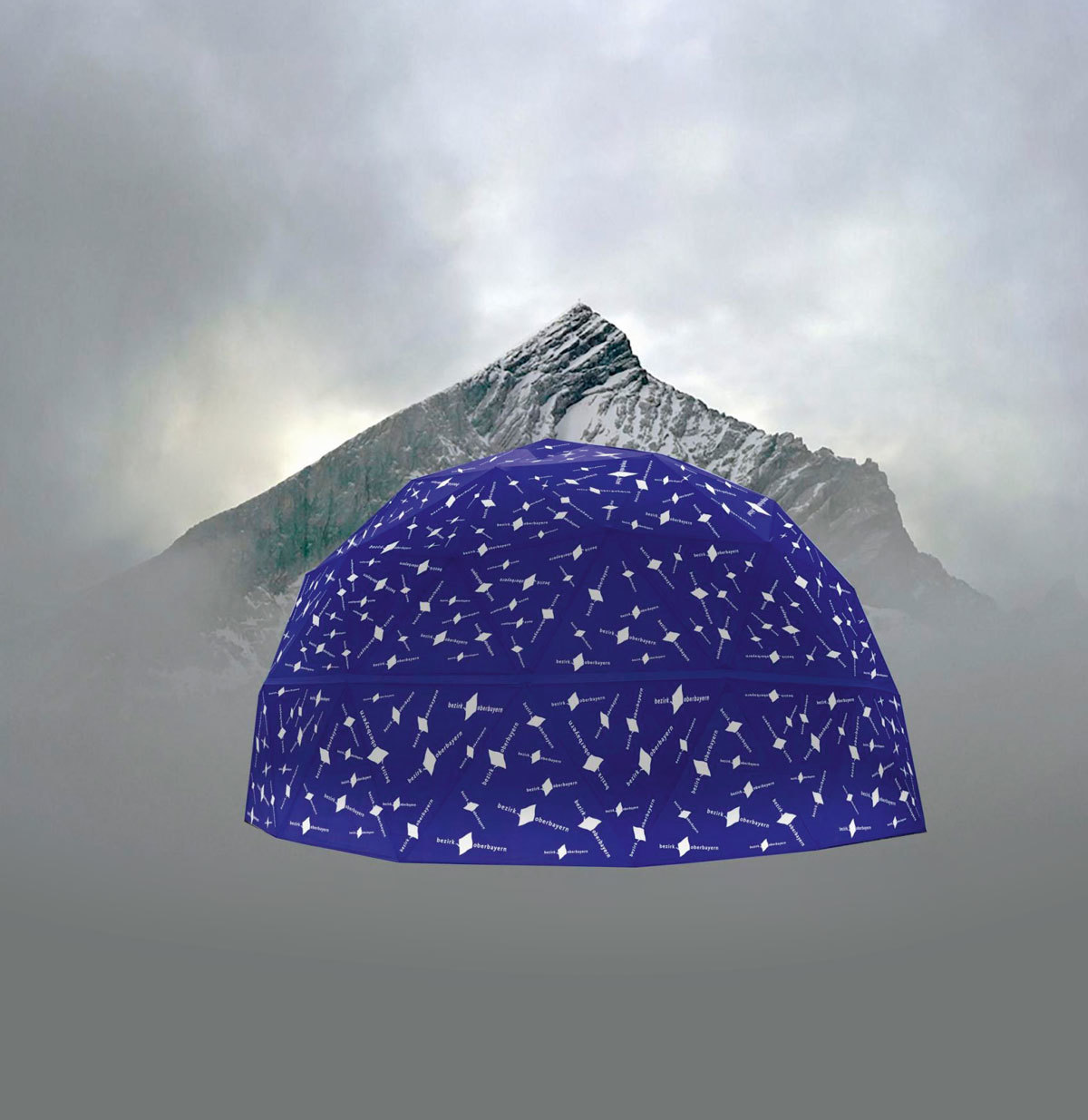 Fotomontage: Eine große blaue Kuppel, die über und über mit dem Logo des Bezirks Oberbayern versehen ist, steht vor einer Bergkulisse.
